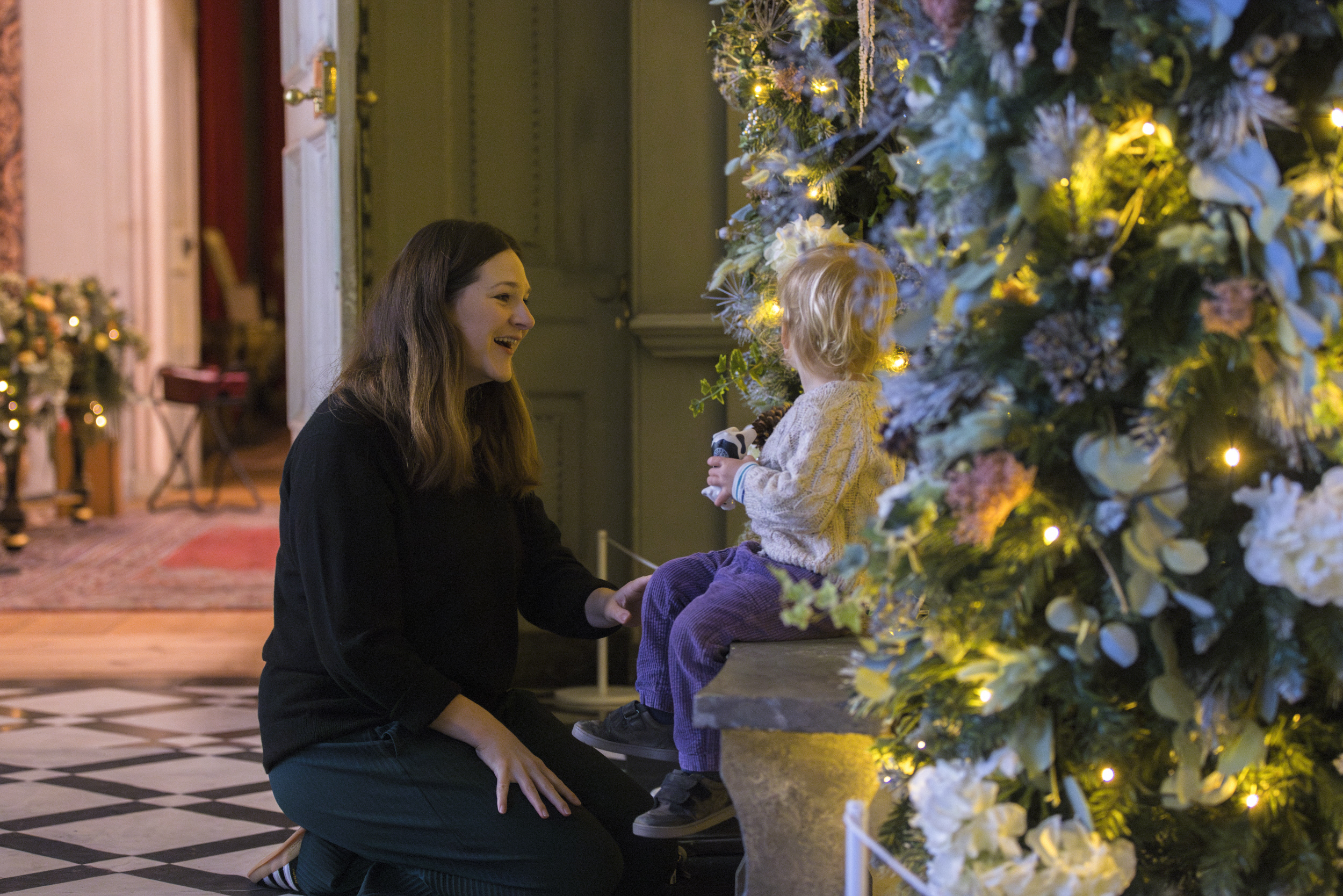 Child sitting on the bench under the colourful archway in the enchanted winter garden in the Marble Hall at Petworth, West Sussex